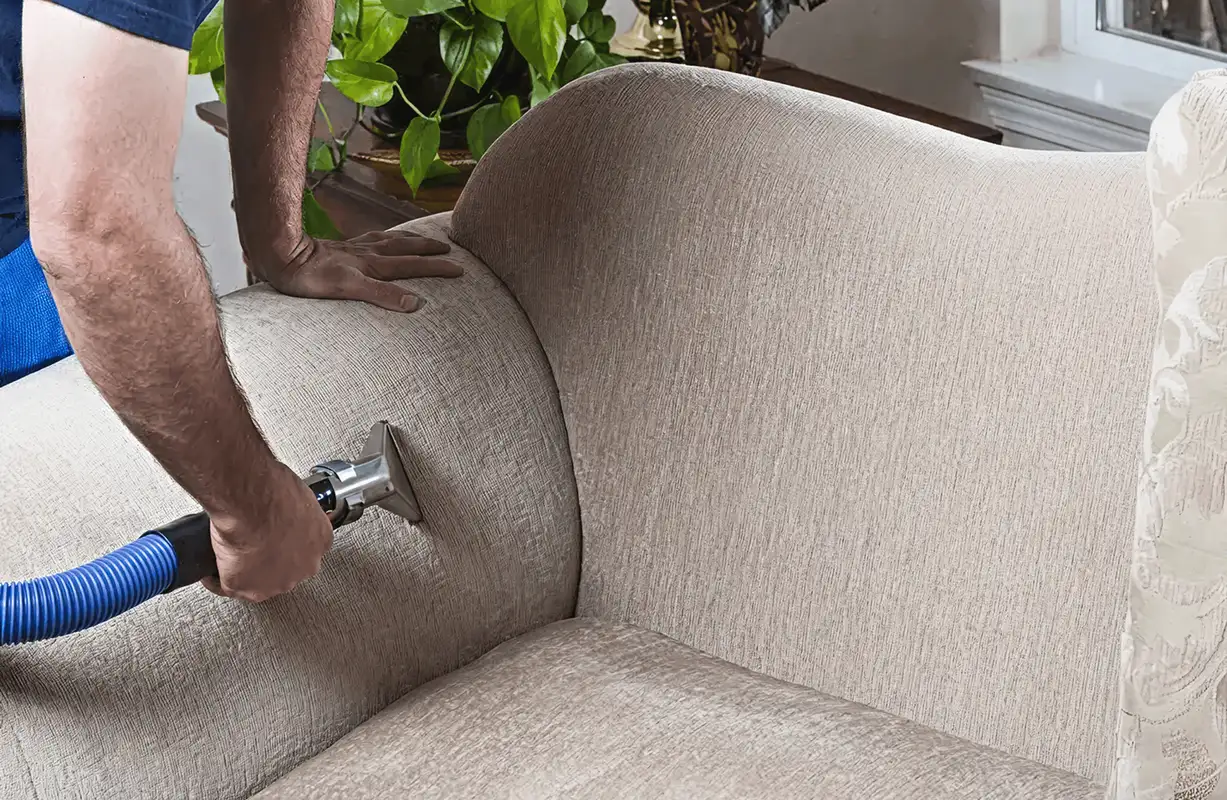 Professional upholstery cleaner deep-cleaning a fabric sofa with a handheld extraction tool and hose, Orlando, FL.